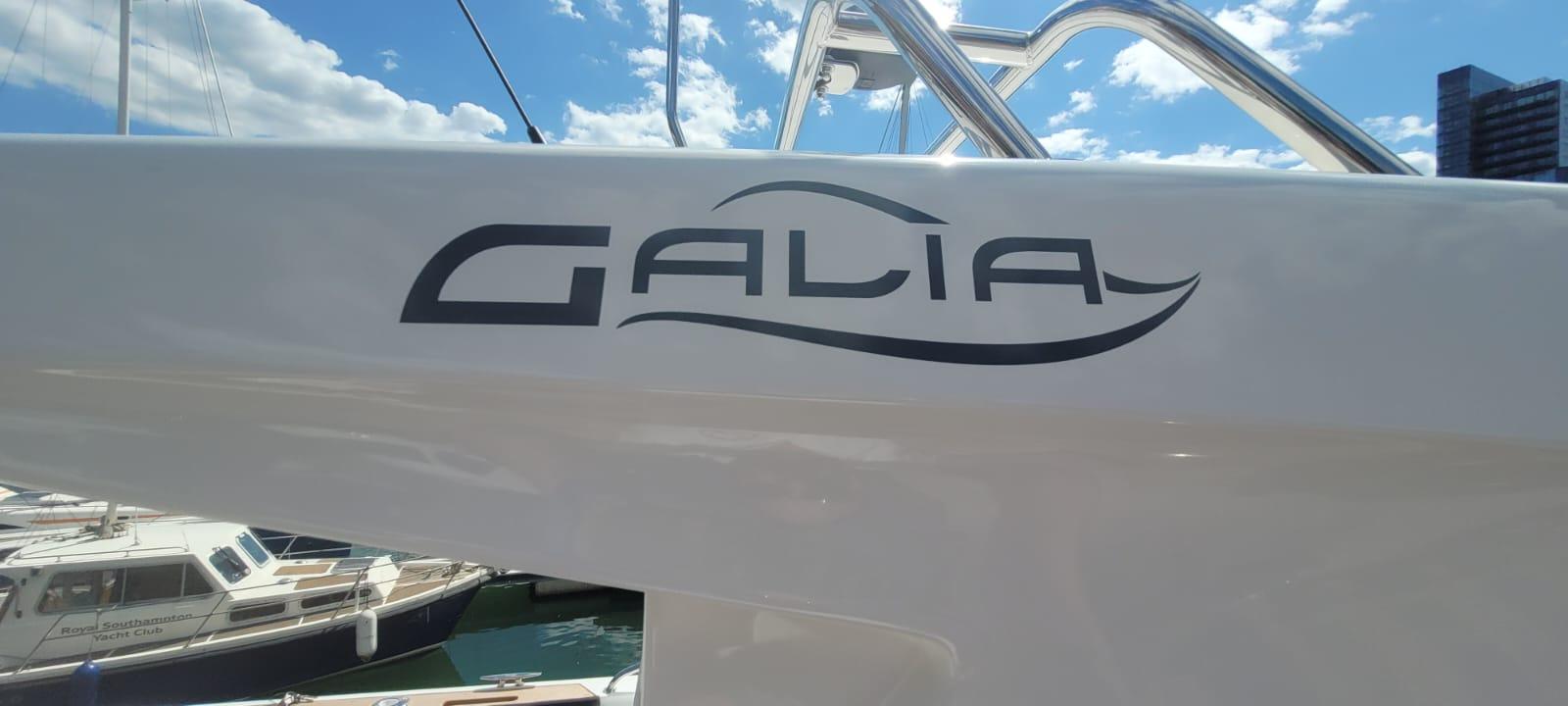 Galia logo displayed on the side of a boat with a blue sky and clouds in the background at a marina.